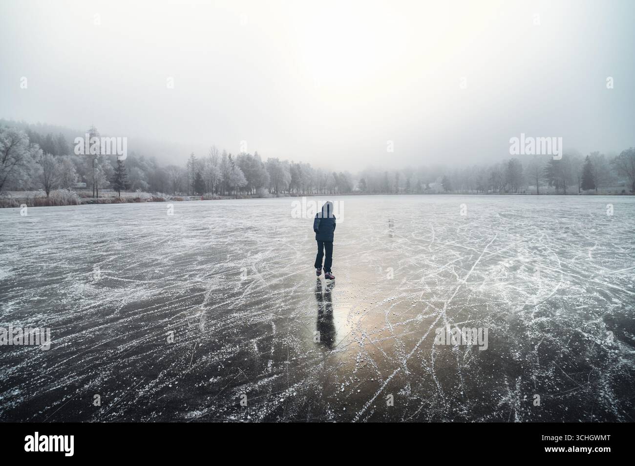 Ein einsames Kind gleitet anmutig auf einem gefrorenen Teich, umgeben von einer weißen, verschneiten Weihnachtslandschaft Stockfoto