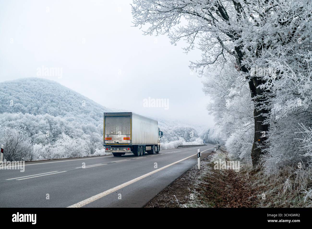 Ein Lkw fährt auf der schneebedeckten Straße durch eine magische weiße Winterlandschaft und liefert Lebensmittel und Vorräte für die Weihnachtszeit Stockfoto