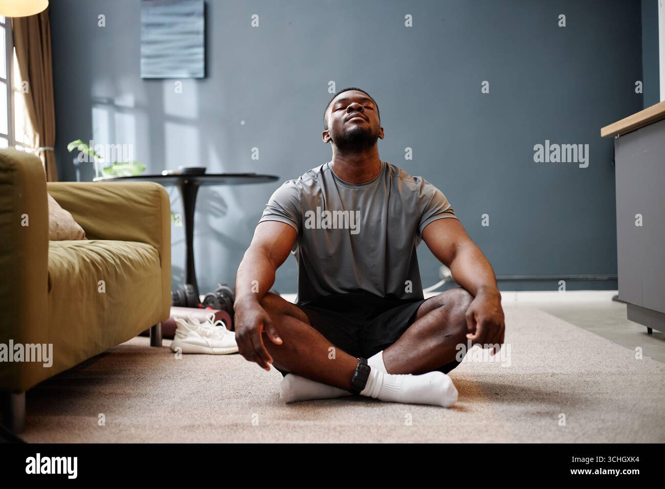 Junger erwachsener Schwarzer Mann, der drinnen meditiert, während der Hausarrest-Situation Stockfoto