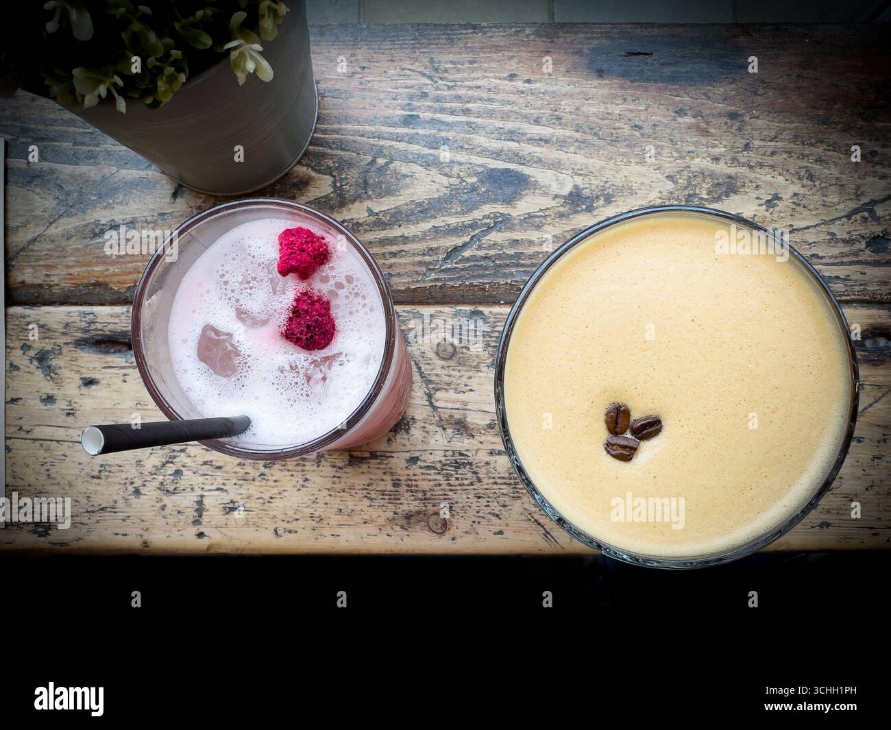 Blick von oben auf zwei alkoholische Cocktails auf einem rustikalen Holztisch, einen rosafarbenen Smoothie mit Himbeeren und einen Espresso-Martini mit Kaffeebohnen Stockfoto