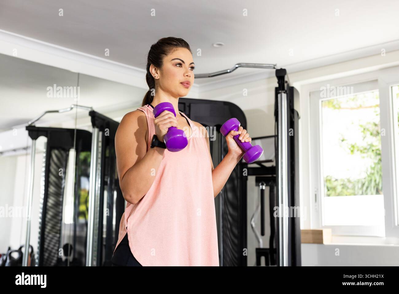 Frau, die lila Kurzhanteln im Fitnessstudio hebt, konzentriert sich auf Krafttraining Stockfoto