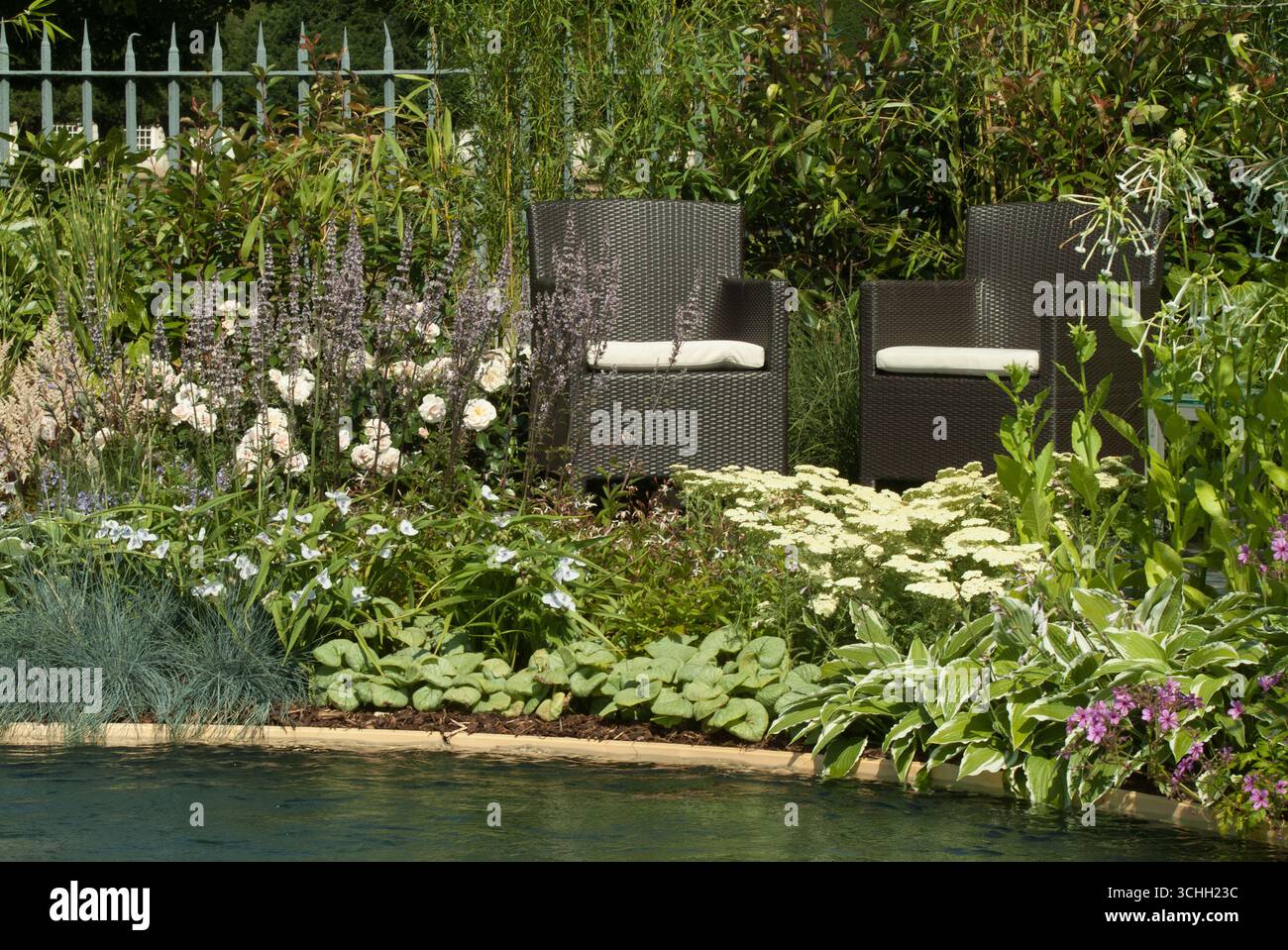 Zwei einladende Stühle befinden sich neben einem ruhigen Pool, umgeben von bunten Blüten und üppigen Pflanzen, die einen perfekten Erholungsort schaffen. Stockfoto