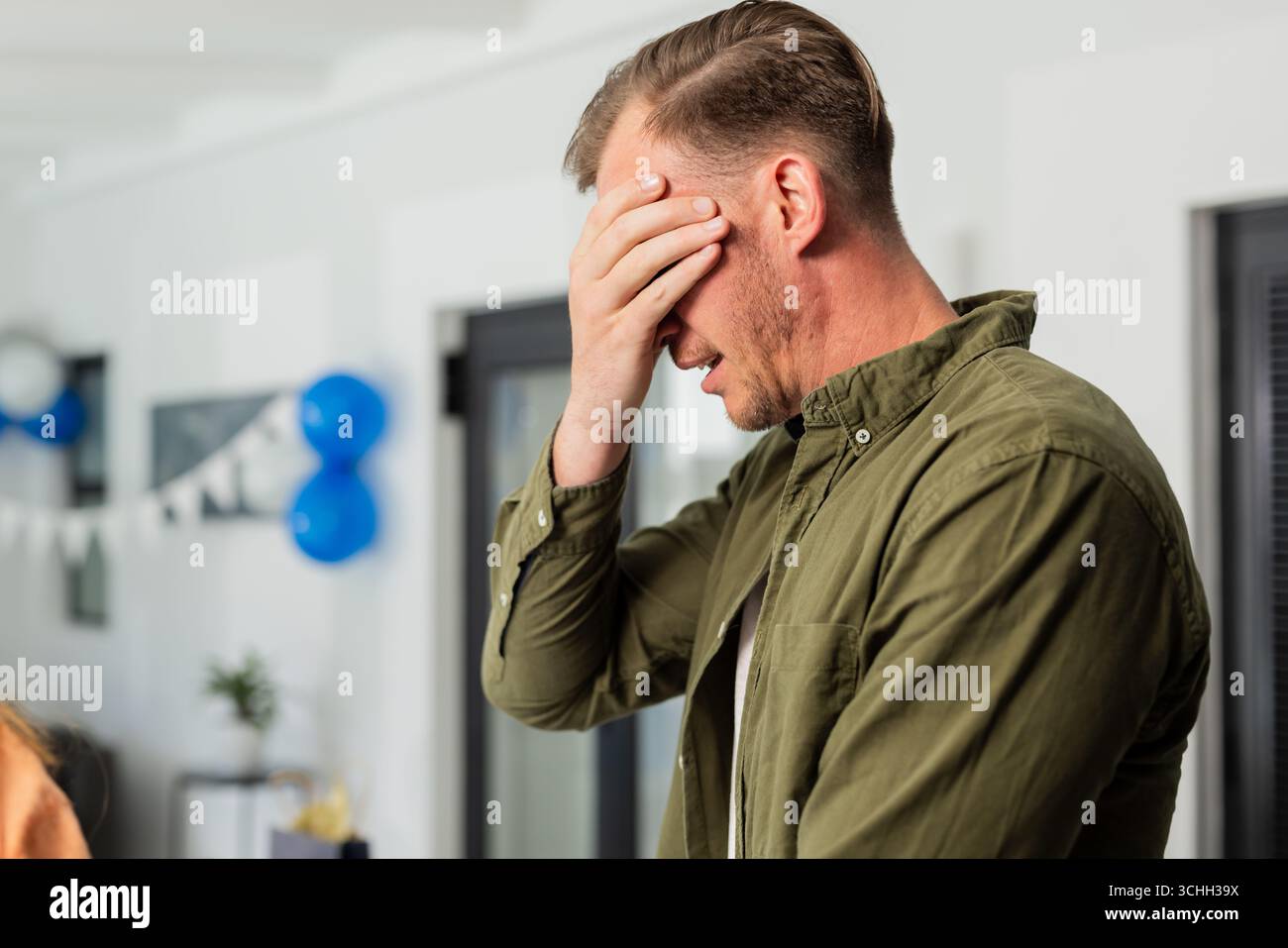 Mann in grünem Hemd, der das Gesicht mit der Hand bedeckt und sich zu Hause überwältigt fühlt Stockfoto