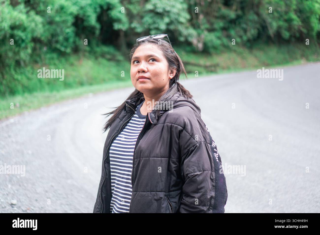 Asiatische Frau mit warmer Jacke und gestreiftem Hemd, die auf der Bergstraße steht Stockfoto