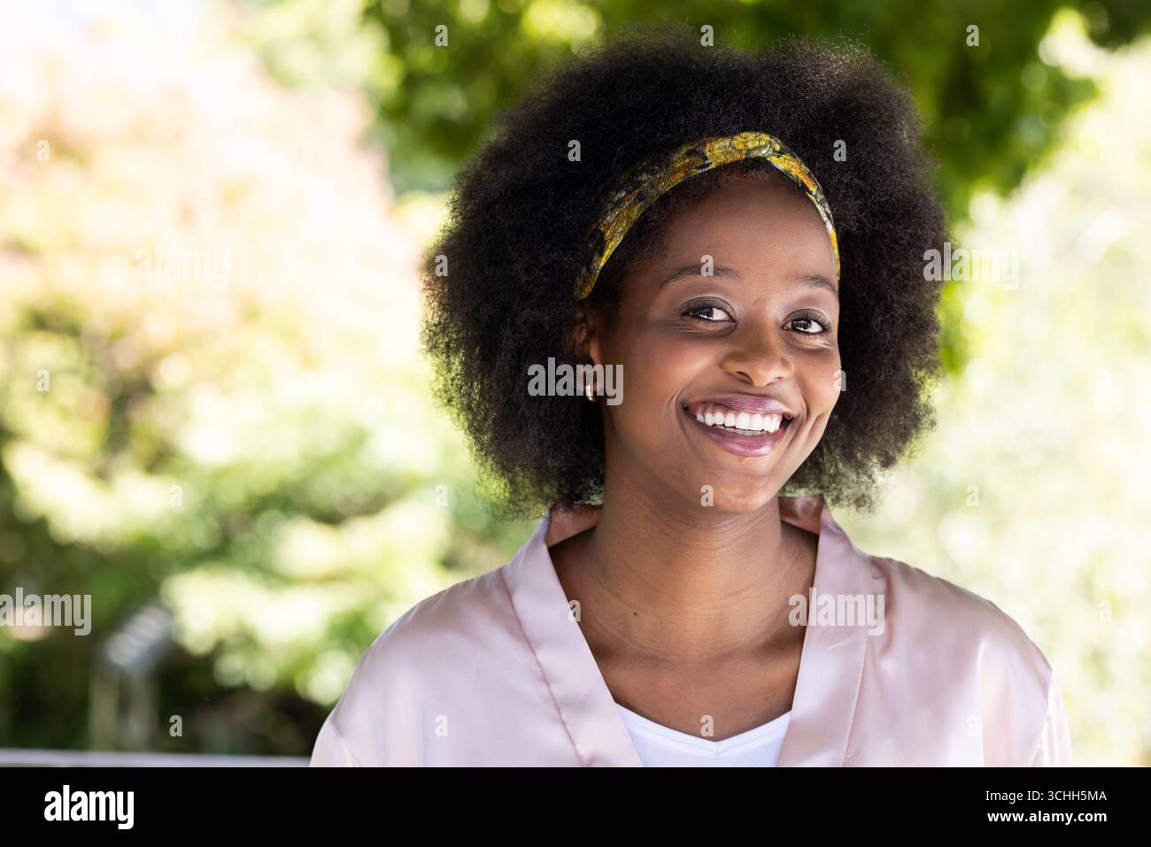 Lächelnde Afroamerikanerin mit Stirnband, sonniger Tag mit natürlichem Hintergrund, Kopierraum Stockfoto