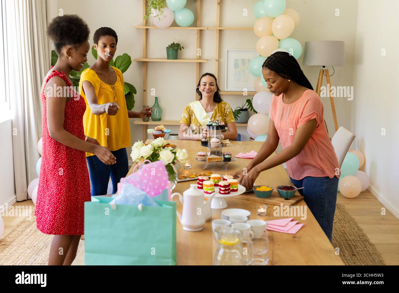 Verschiedene Freundinnen bereiten einen Tisch mit Desserts und Getränken für die Feier zu Hause vor Stockfoto