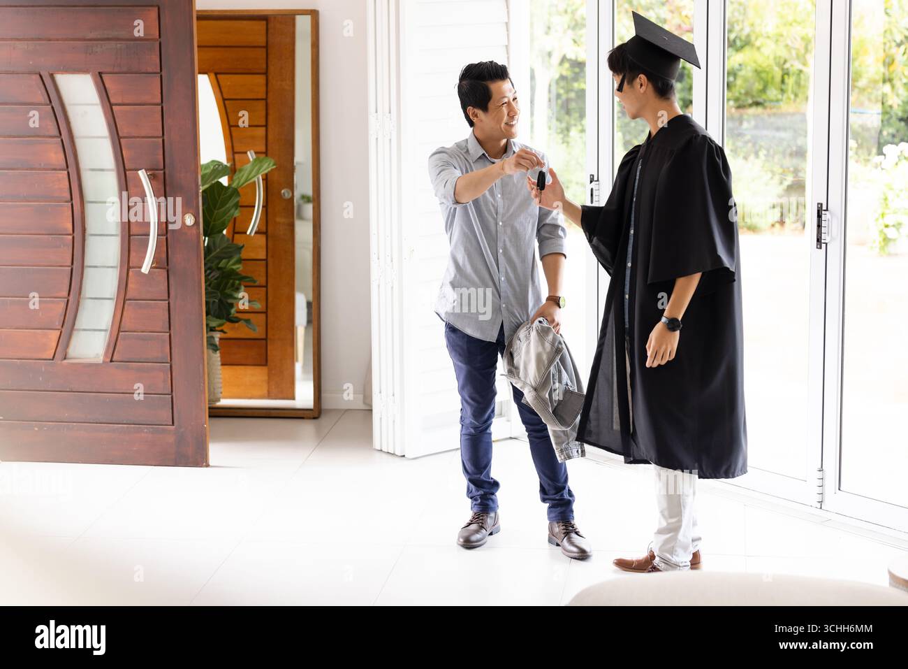 Stolzer Vater gratuliert seinem Sohn im Abschlusskleid zu Hause und teilt einen freudigen Moment Stockfoto