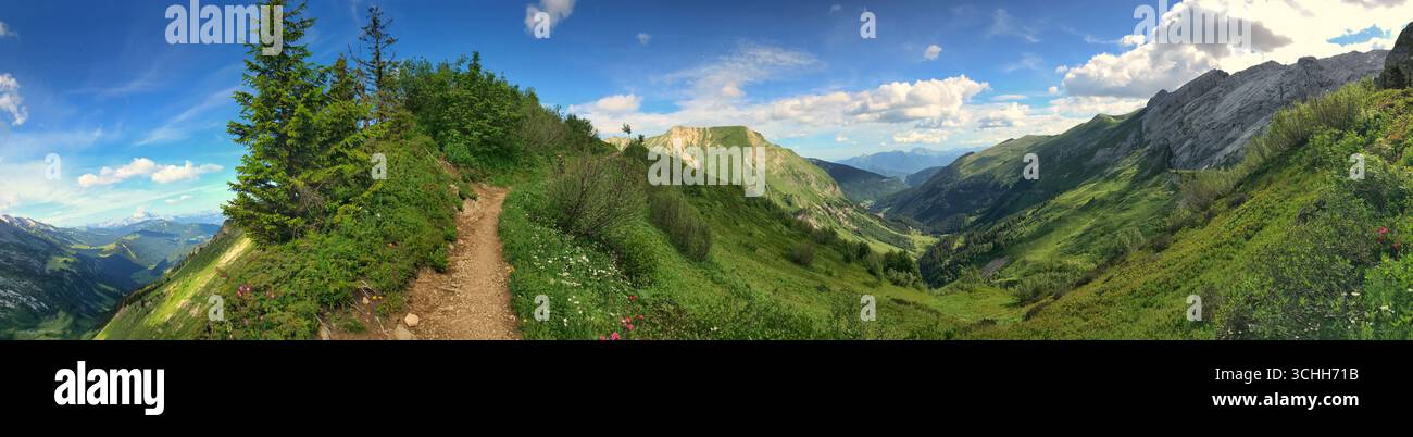 Großer Panoramablick auf die üppigen grünen Berge, einen malerischen Wanderweg und den lebendigen Himmel. Ideal für Inspirationen in der Natur, Landschaften, Reisen und Outdoor-Aktivitäten Stockfoto