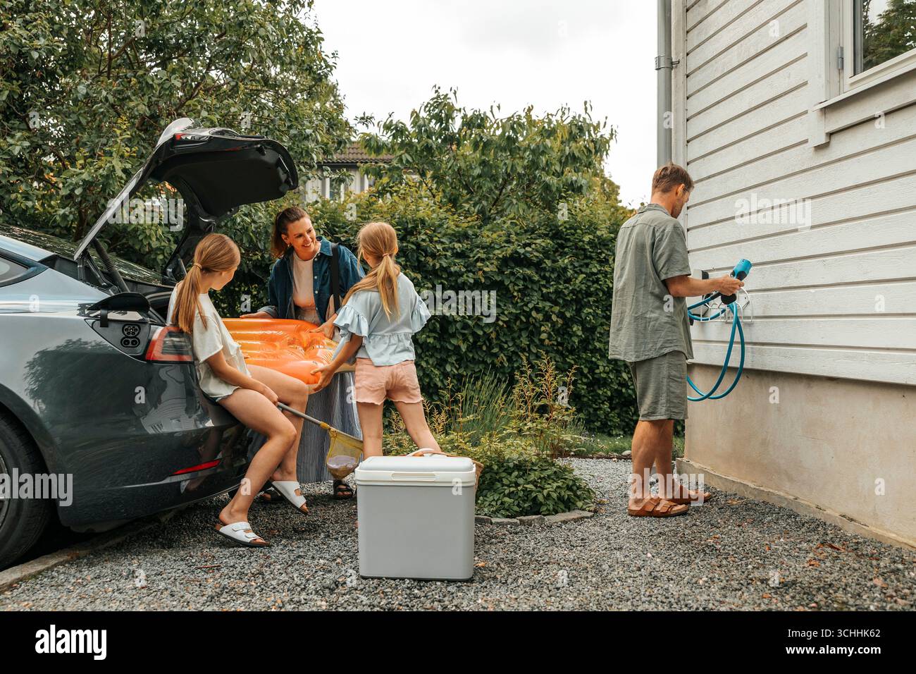 Die Familie bereitet sich auf den Roadtrip vor, indem sie den Kofferraum im Hinterhof verstaut Stockfoto