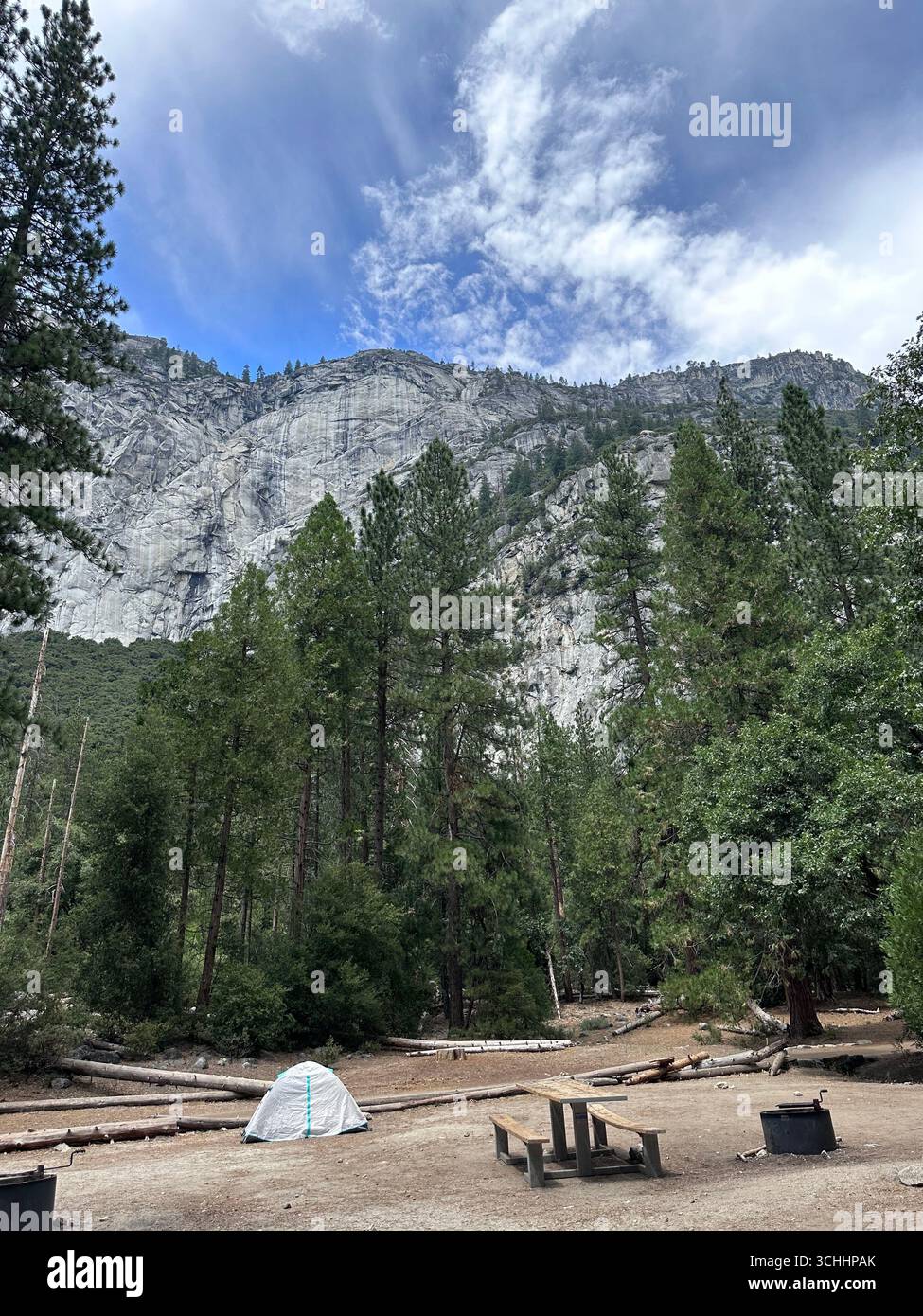 Ein kleines Campingzelt im Yosemite-Nationalpark, umgeben von hohen Kiefern mit hoch aufragenden Granitklippen im Hintergrund unter einem teilweise Clo - Smartphone-aufgenommenes Stockfoto