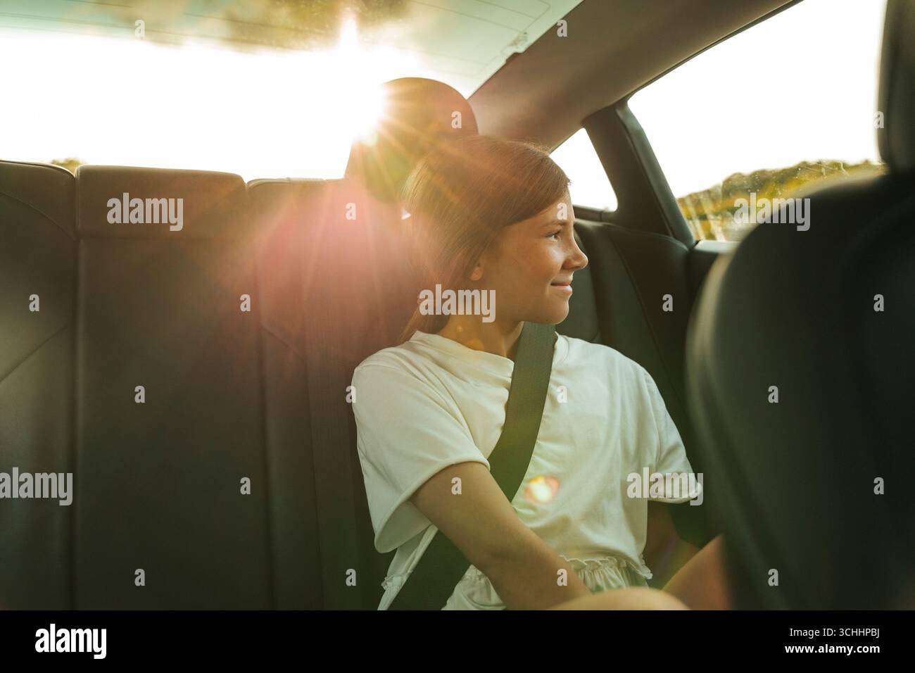 Sonnenlicht scheint durch das Glas auf lächelndes Mädchen, das im Auto sitzt und den Sicherheitsgurt für einen Roadtrip hat Stockfoto
