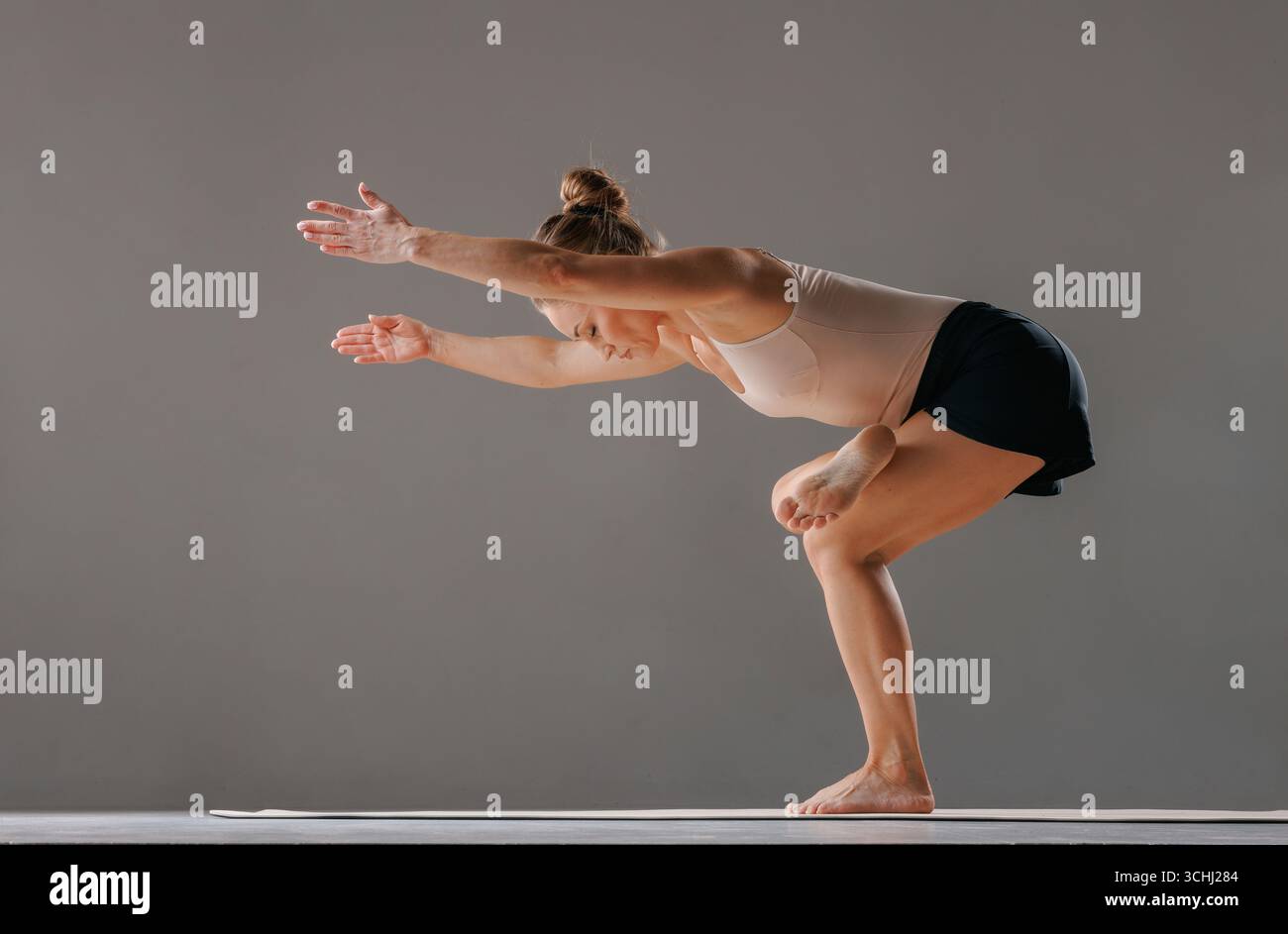 Athletische Frau balanciert in einer stehenden Yoga-Haltung mit ausgestreckten Armen, die Flexibilität und Körperkontrolle zum Ausdruck bringt. Stockfoto