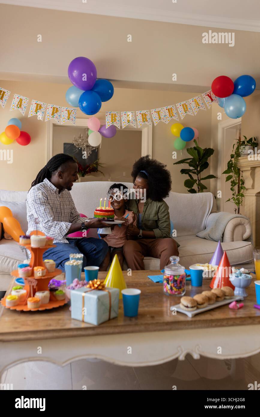 Geburtstag feiern, Eltern geben dem Kind zu Hause Kuchen mit farbenfrohen Dekorationen Stockfoto