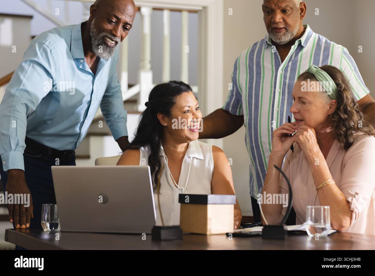 Senioren treffen sich zu Hause um den Laptop, teilen sich fröhliche Gespräche und Lachen Stockfoto