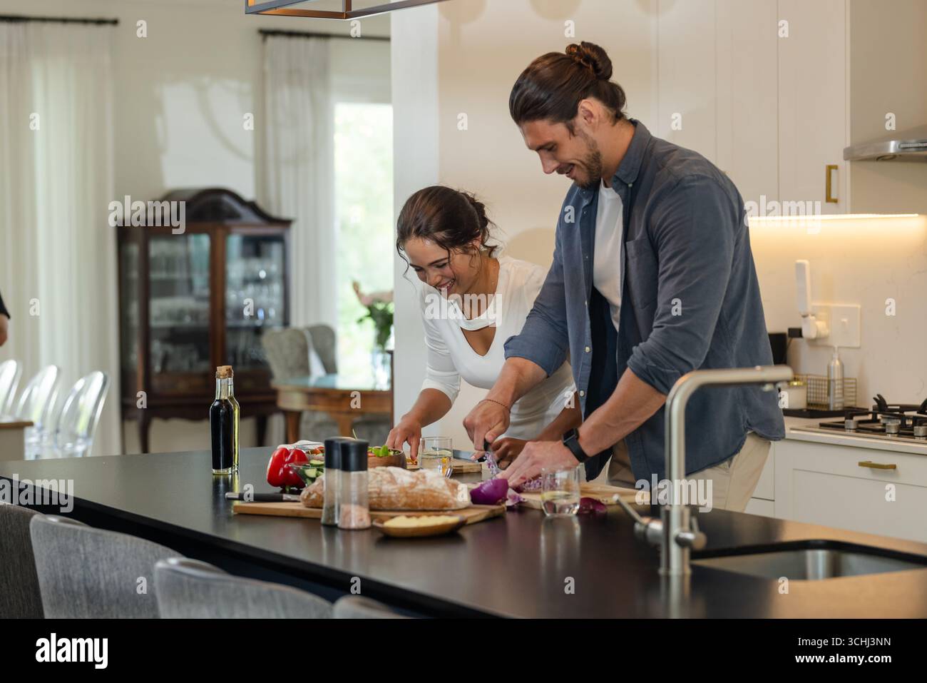 Ein Paar, das zusammen in der modernen Küche Essen zubereitet, lächelt und genießt das Kochen Stockfoto