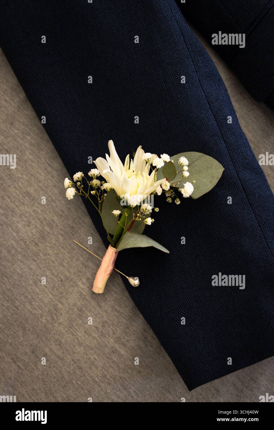 Elegante Boutonniere mit weißer Blume und Grün auf dunkler Anzugsjacke Stockfoto