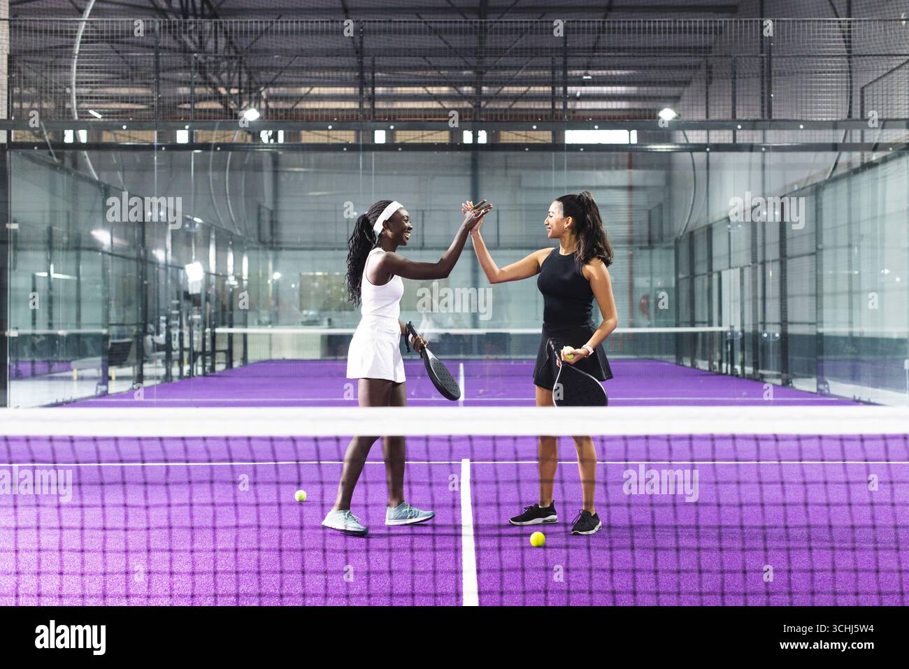 Diverse Athleten auf dem lila Paddle Court mit Schlägern, Tennisbällen, weißem Netz Stockfoto