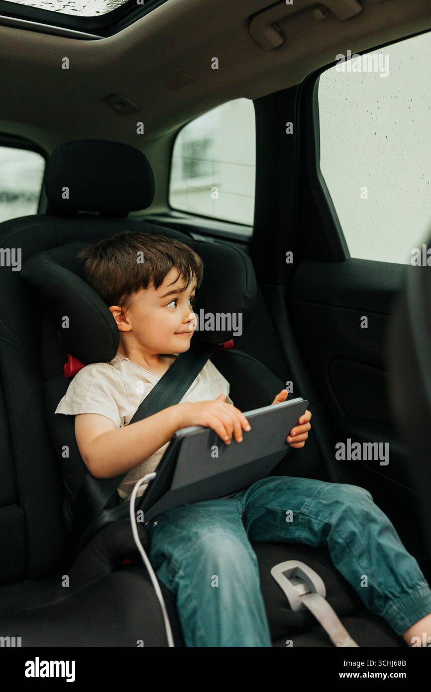 Junge, der durch das Fenster schaut, während er während des Wochenendausflugs auf einem Autositz sitzt Stockfoto