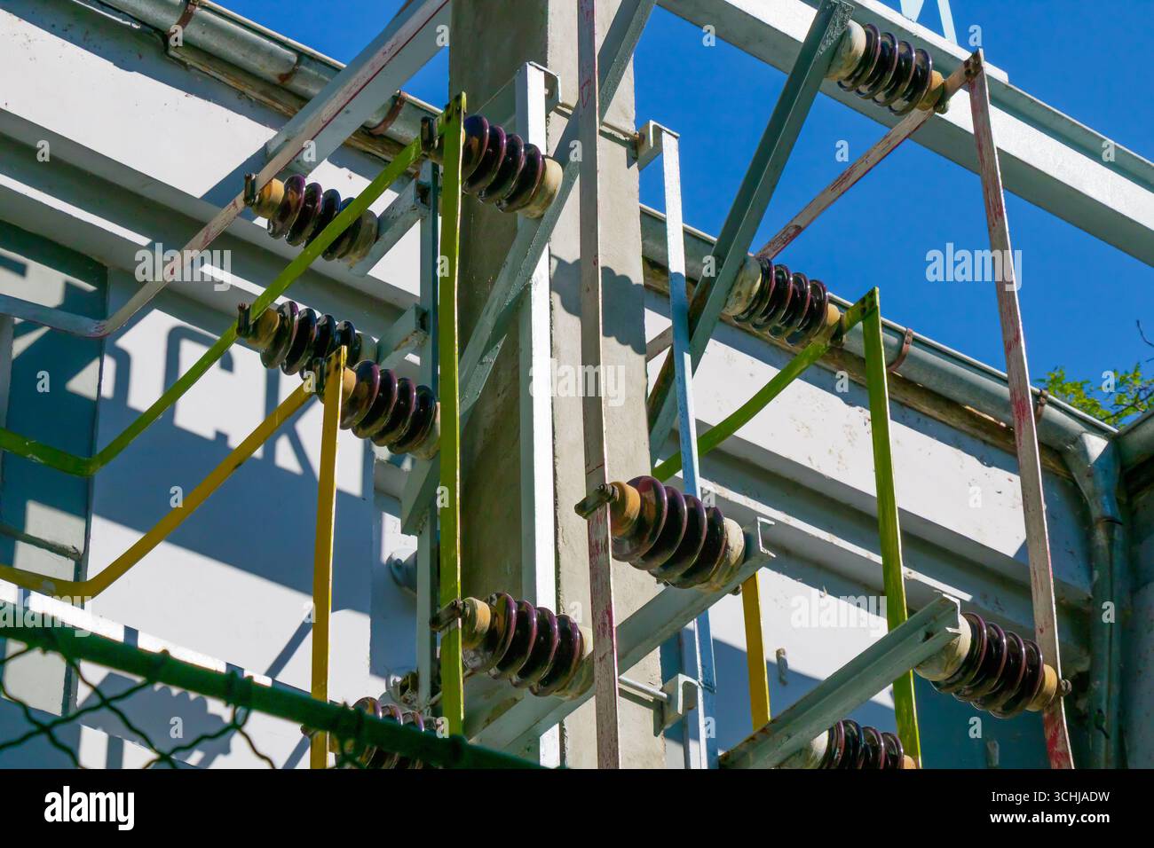 Farbenfrohe Isolatoren und Kabel verbinden sich auf einer Struktur, die das komplizierte Design der elektrischen Infrastruktur unter einem hellblauen Himmel unterstreicht. Das Set Stockfoto