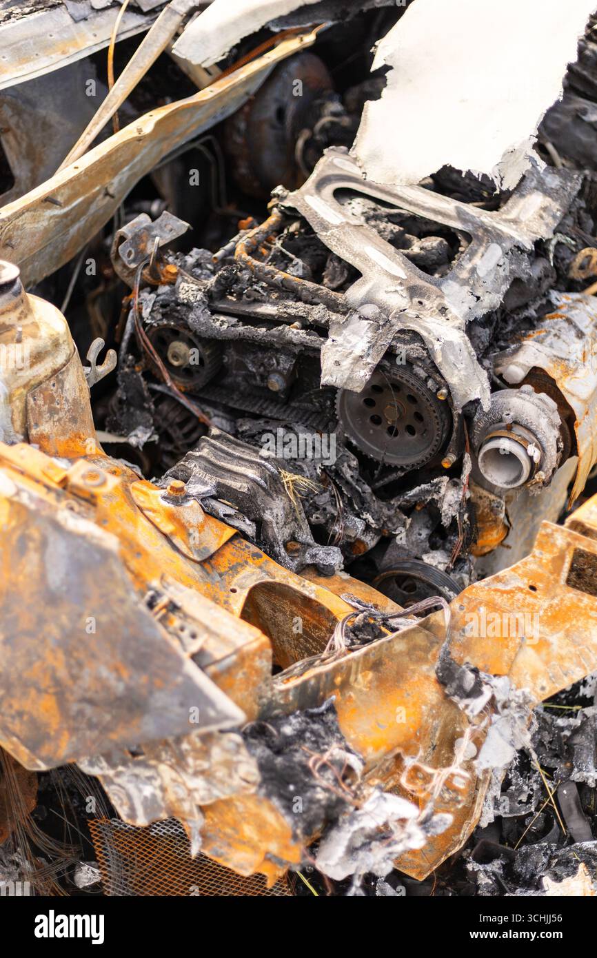 Ein stark verkohltes Fahrzeug befindet sich auf einem grasbewachsenen Gebiet und legt die beschädigten Motorkomponenten frei. Die Szene vermittelt Vernachlässigung und die Folgen eines Feuers Stockfoto