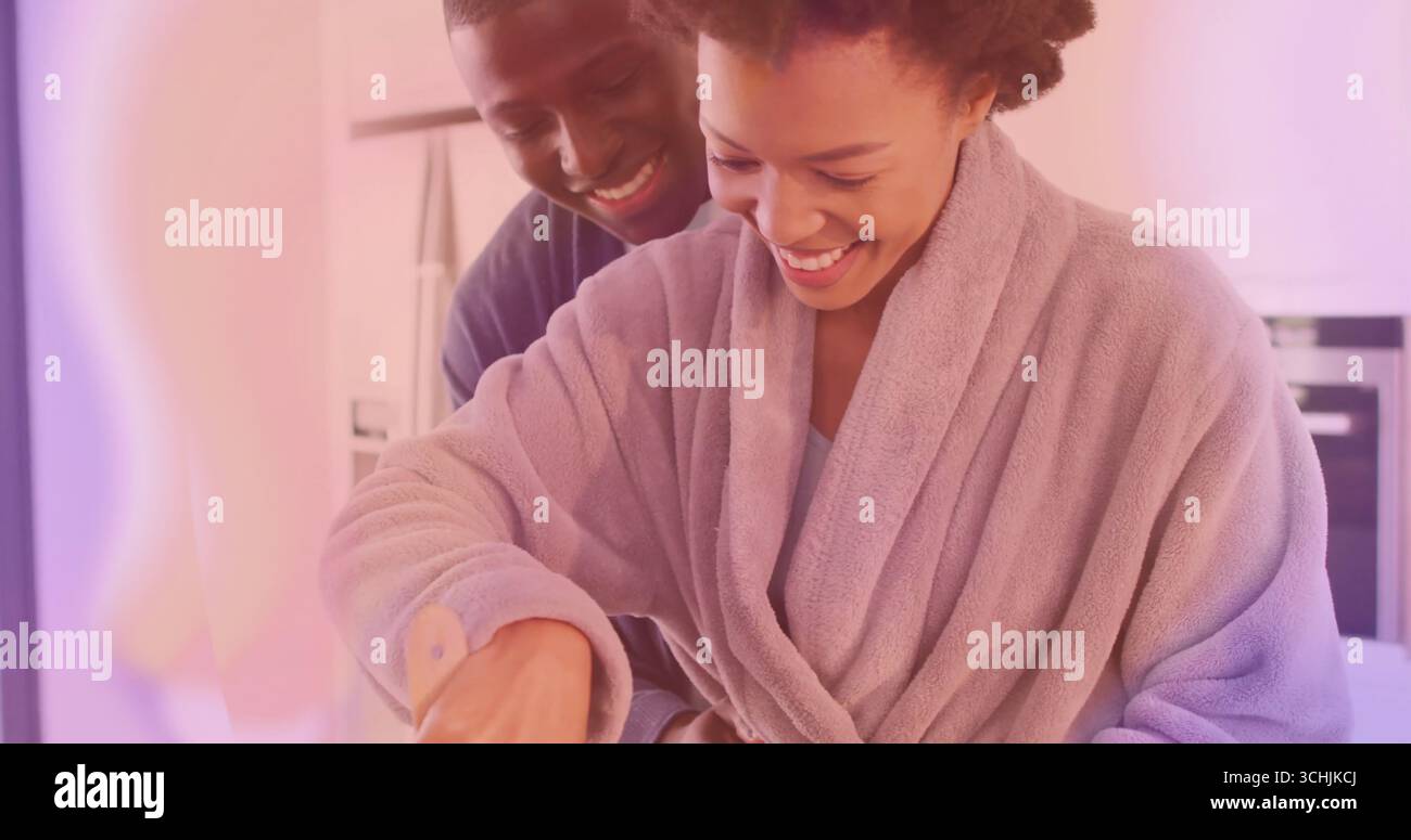 Bademantel trägt Frau, die mit lächelndem Partner in der Küche kocht, mit Holzspachtel und Mischschüssel Stockfoto