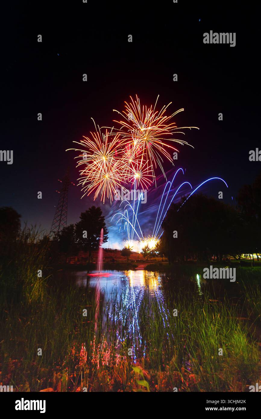 Ein helles Feuerwerk bricht in leuchtenden Farben über einem ruhigen See und reflektiert während eines Sommerfestes auf dem Wasser. Stockfoto