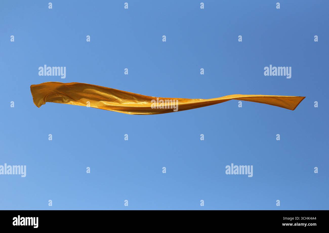 Ein lebhaftes gelbes Stoffbanner schwingt anmutig im klaren blauen Himmel und symbolisiert Bewegung und Lebendigkeit. Stockfoto