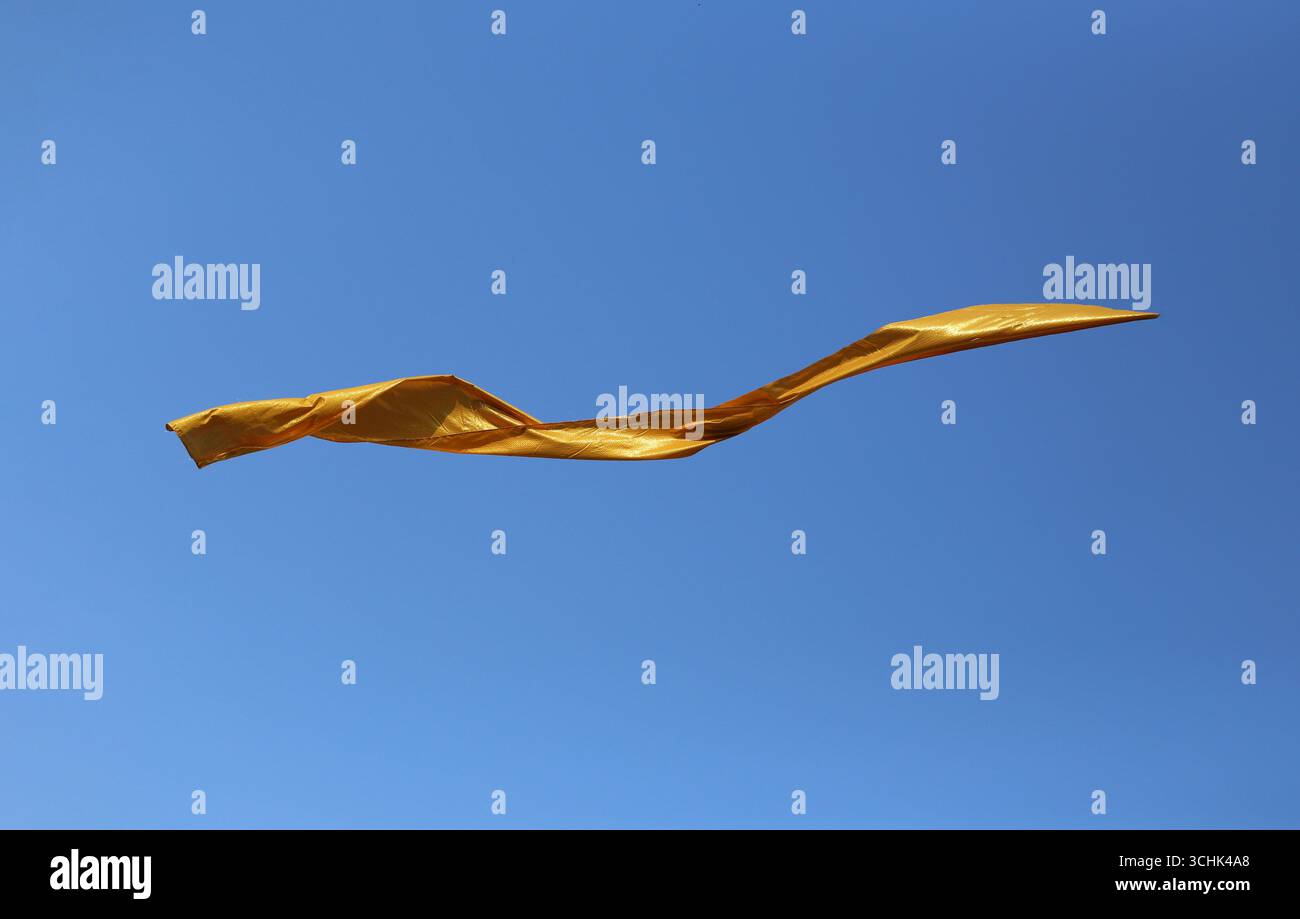 Ein leuchtendes goldenes Band tanzt durch einen klaren blauen Himmel und symbolisiert Freiheit und Freude. Diese atemberaubende Farb- und Lichtdarstellung sorgt für ein aufmunterndes und Stockfoto