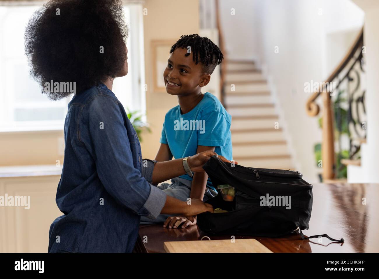 Mutter und Kind packen Rucksack zu Hause und teilen einen freudigen Moment zusammen Stockfoto