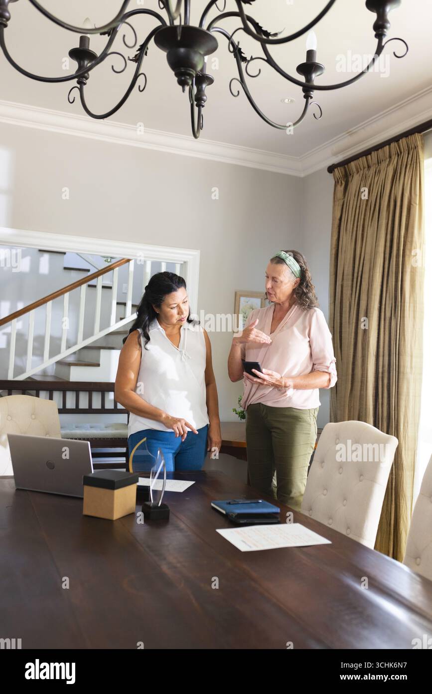 Zwei Frauen diskutieren über die Arbeit zu Hause, indem sie Smartphone und Laptop auf dem Tisch benutzen Stockfoto
