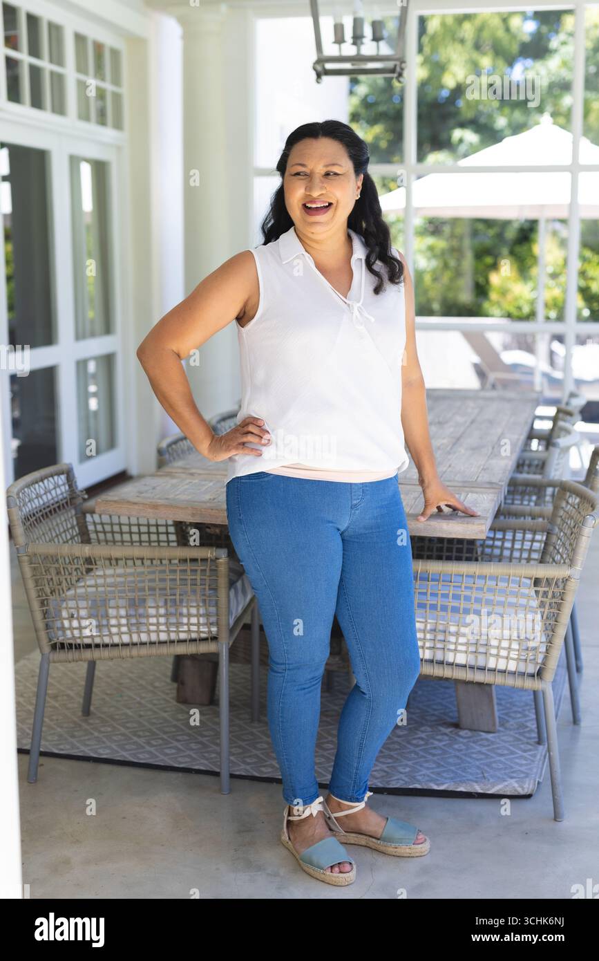 Lächelnde Frau, die auf der Terrasse steht und den sonnigen Tag in lässigem Outfit genießt Stockfoto