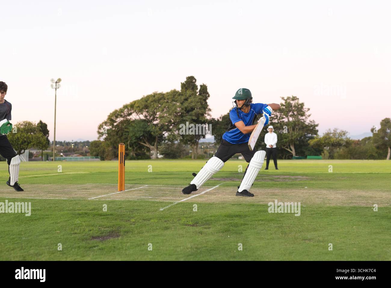 Teenager-Schlagmann in blauem Hemd, der mit Cricketschläger auf dem Rasenplatz einen Schuss spielt, Kopierraum Stockfoto