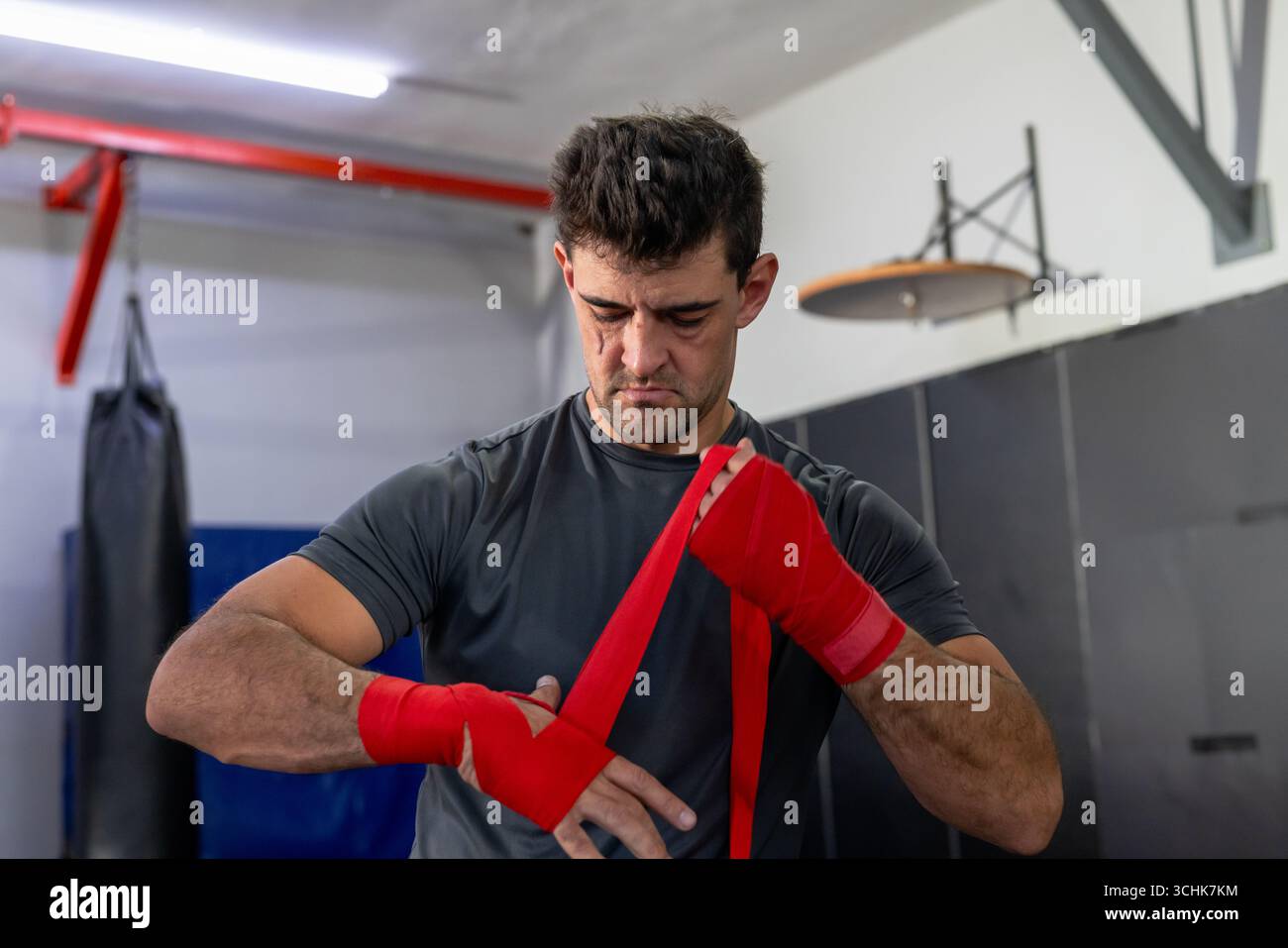 Mann, der Hand um die Handgelenke wickelt, im Boxstudio mit schwerer Tasche, Speed Bag Plattform Stockfoto