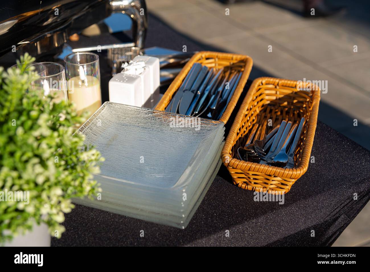 Ein Restaurant im Freien mit Glasplatten, Besteck in Korbkörben und Kerzen schafft eine elegante Atmosphäre. Ideal für elegante Versammlungen Stockfoto