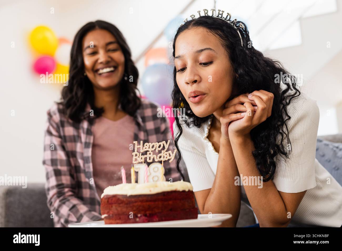 Zu Hause, Teenager-Mädchen, die Kerzen auf Geburtstagskuchen ausbläst, lächelnde Mom, die zusammen feiert Stockfoto