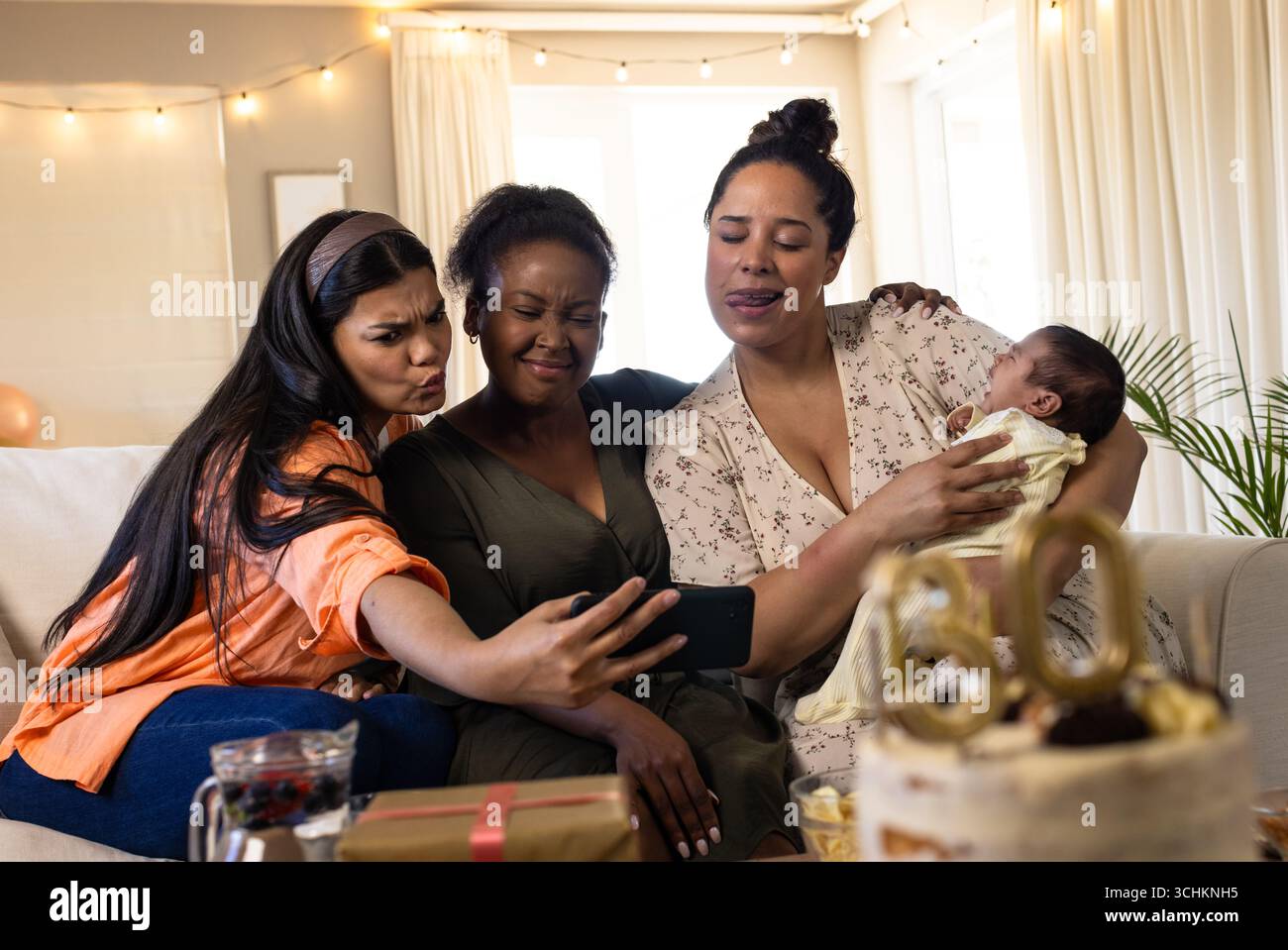 Verschiedene Freundinnen machen Selfie auf der Couch, feiern mit Kuchen und neugeborenes Baby zu Hause Stockfoto