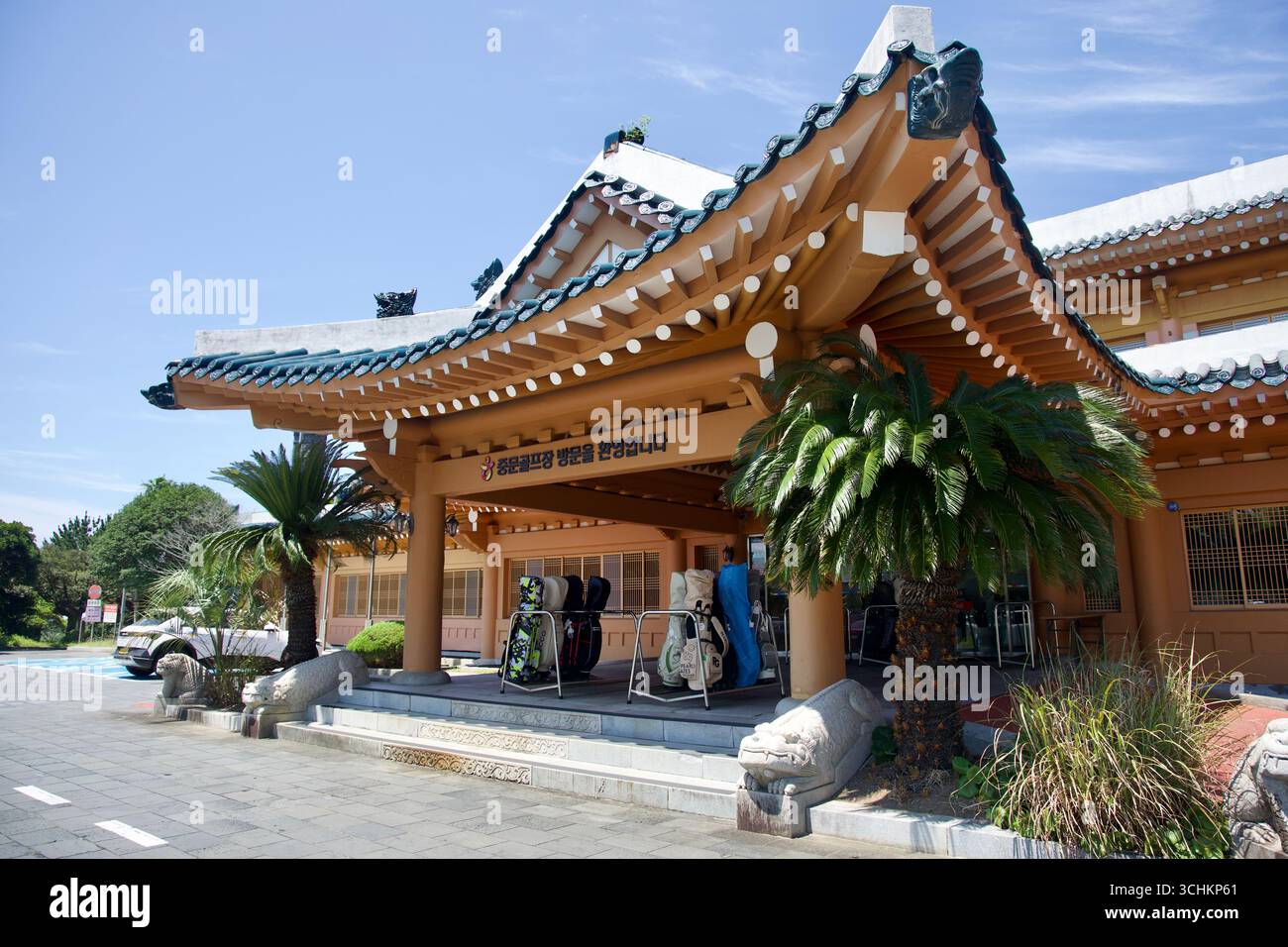 Das Clubhaus des Jungmun Golfplatzes zeigt ein weitläufiges Dach im hanok-Stil über dem Eingang, mit Golftaschen auf Racks, Steinskulpturen und Tropen Stockfoto