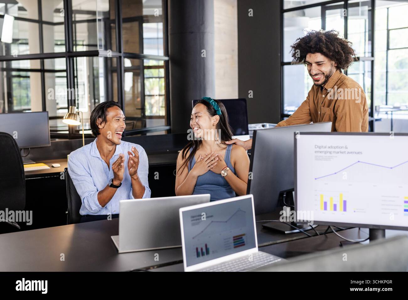 Vielfältiges Team feiert Erfolge in modernen Büros mit Computern und Diagrammen Stockfoto