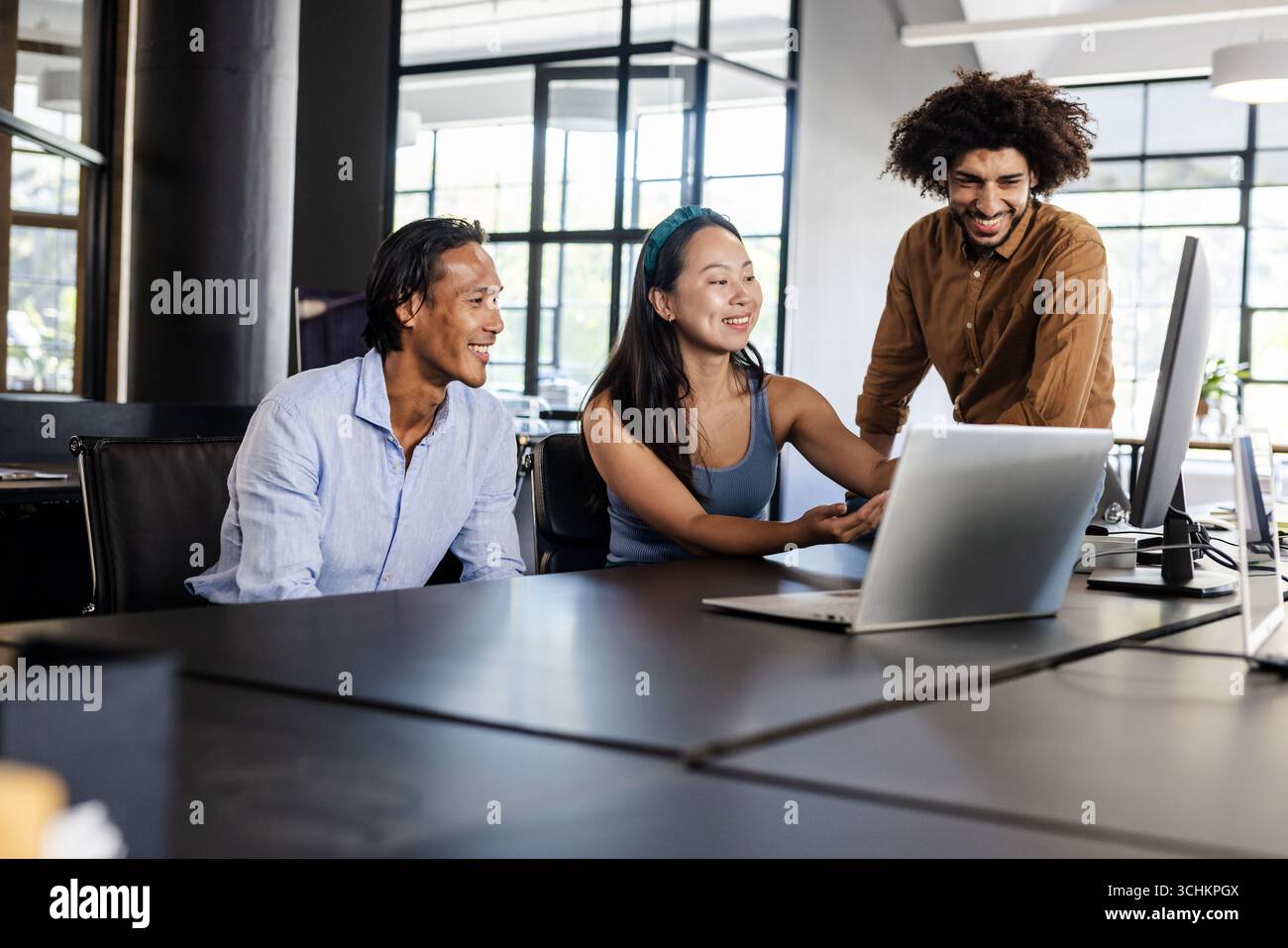 Vielseitiges Geschäftsteam, das in modernen Büros mithilfe eines Laptops an Projekten arbeitet Stockfoto