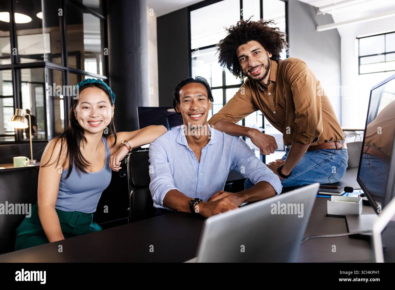 Vielseitiges Geschäftsteam arbeitet am Schreibtisch zusammen, lächelt und selbstbewusst Stockfoto