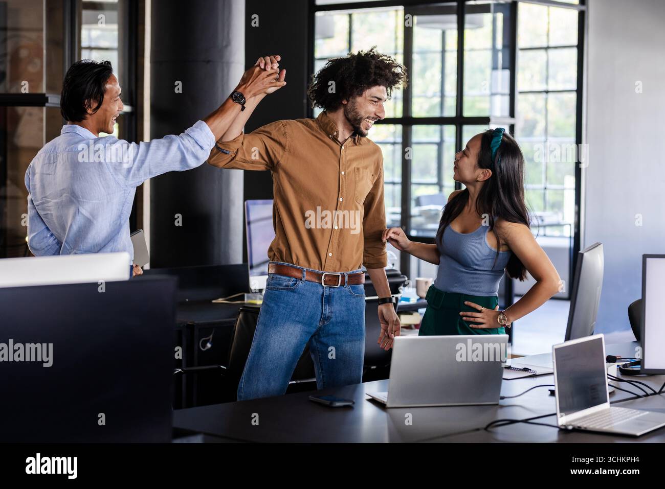 Vielseitiges Team feiert Erfolg im modernen Büro mit Laptops auf dem Schreibtisch Stockfoto