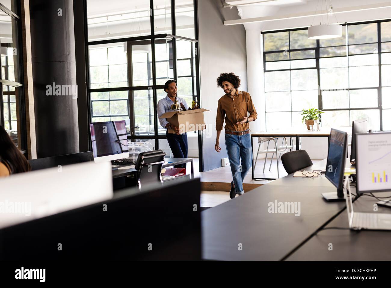 Verschiedene Kollegen, die Kisten transportieren und lächeln, während sie in moderne Büroflächen umziehen Stockfoto