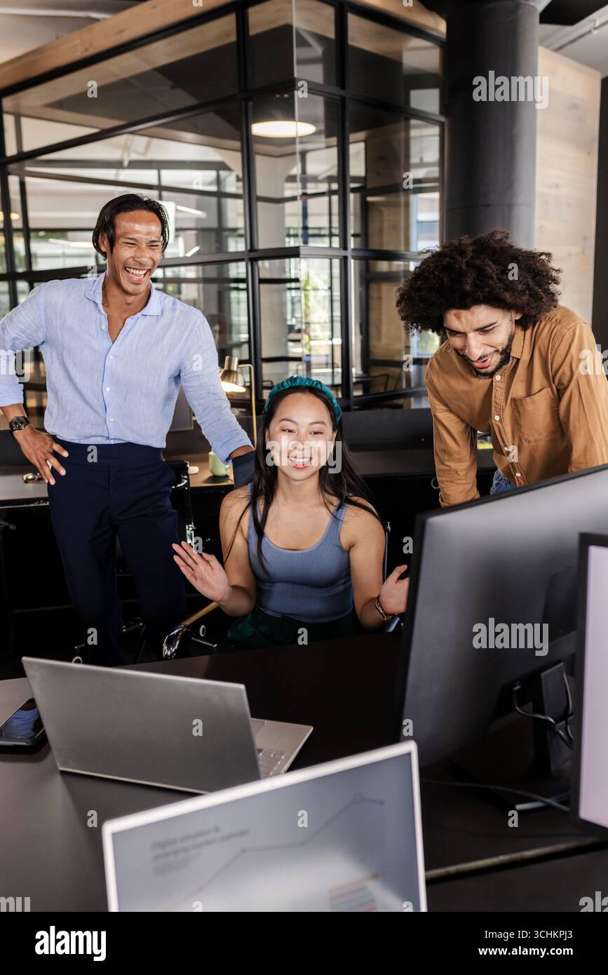 Ein vielfältiges Team, das sich mit Begeisterung um Computerbildschirme in modernen Büros kümmert Stockfoto