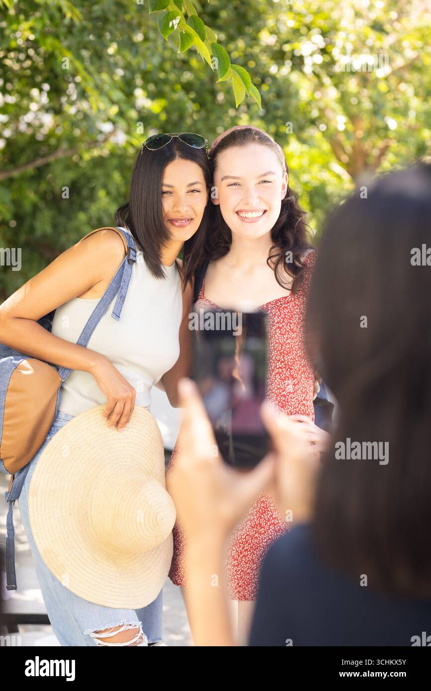 Zwei junge Frauen, eine mit langen dunklen Haaren und eine mit hellbraunem Haar, posieren fröhlich draußen auf s Stockfoto