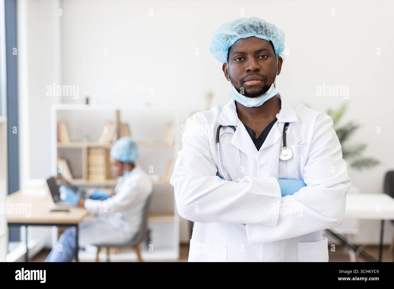 Selbstbewusster männlicher Arzt mit Schutzkleidung im Krankenhaus gekreuzte Arme Stockfoto