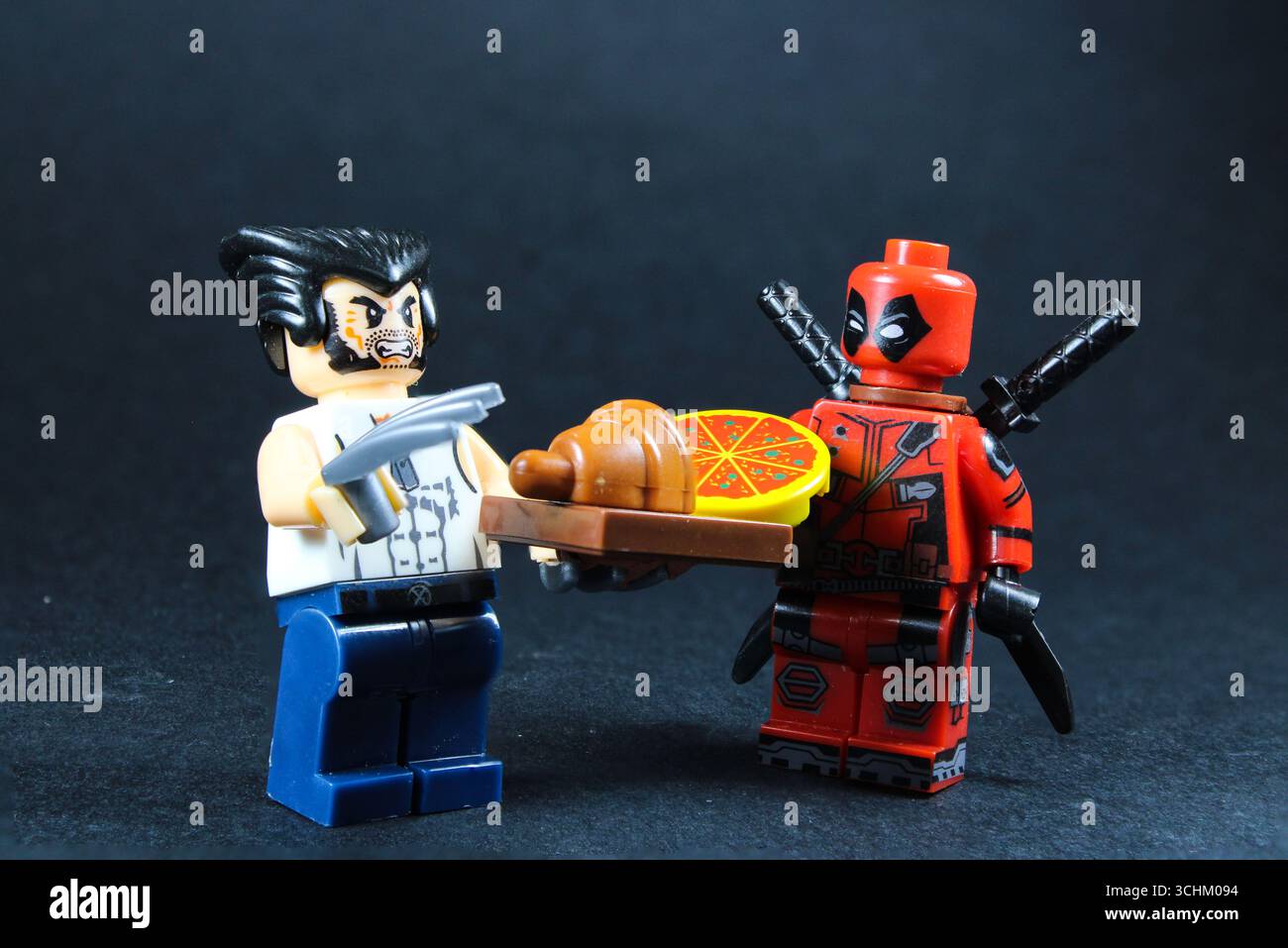 LEGO Wolverine und Lego Deadpool genießen gemeinsam Croissant und Pizza Stockfoto