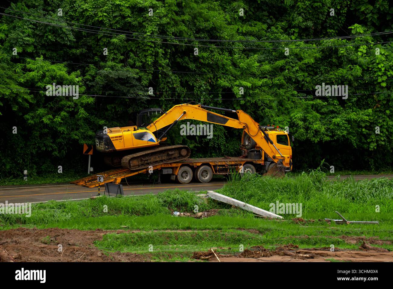 Gelber Bagger auf einem Tieflader-Anhänger während des Hochwasserbetriebs. Schwermaschinen, die für Straßenreparaturen und Katastrophenhilfe in transportiert werden Stockfoto