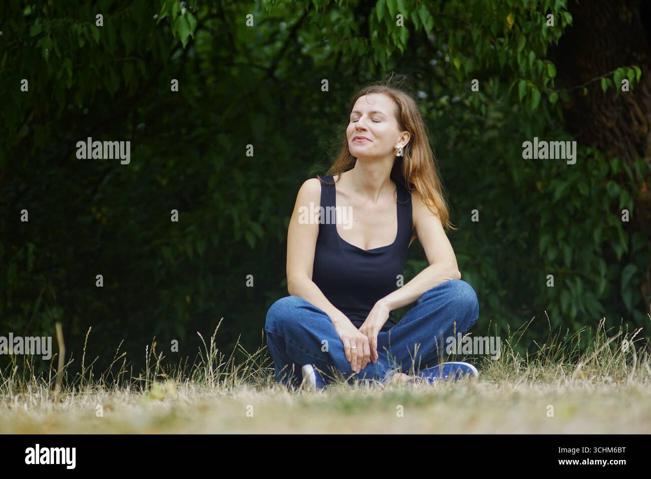 Frau, die im Freien meditiert, umgeben von Grün. Symbol der Achtsamkeit, Waldbaden, digitale Entgiftung, umweltfreundlicher Lebensstil, Bewusstsein für psychische Gesundheit Stockfoto