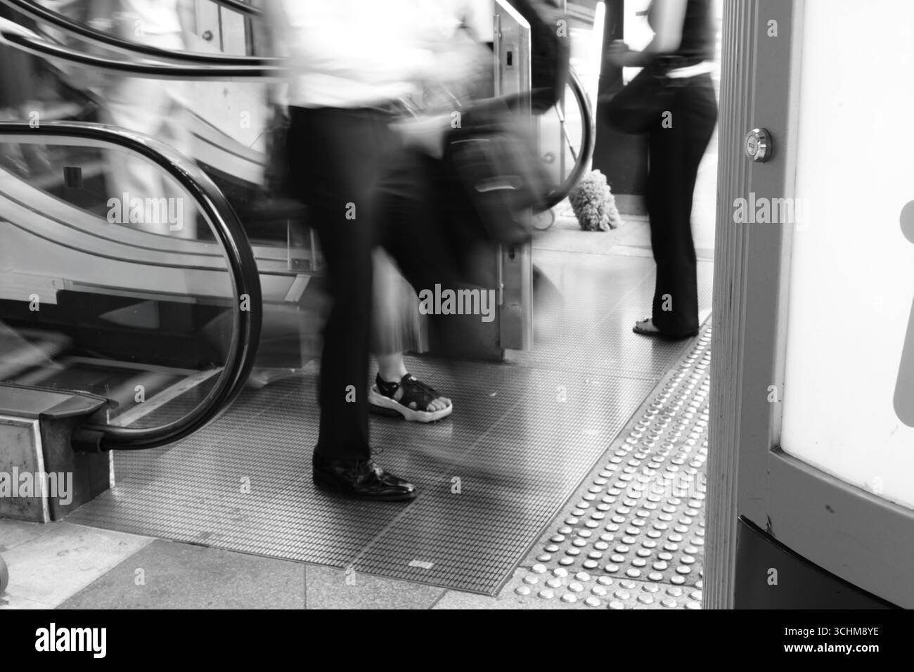Verschwommene Geschäftsleute verlassen eine Rolltreppe in einem stark frequentierten städtischen Raum und spiegeln so den Rhythmus des beruflichen Alltags wider. Stockfoto