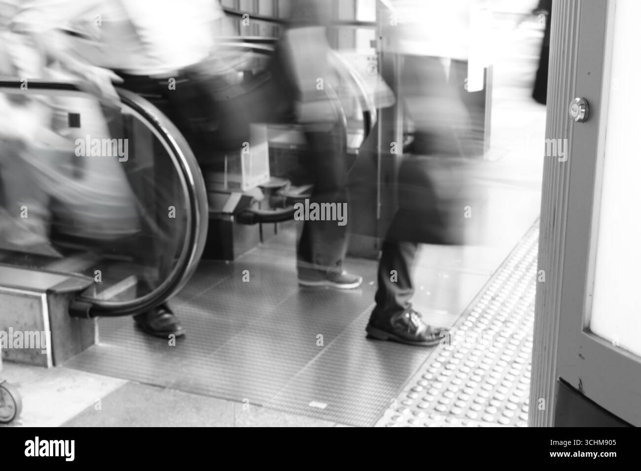Verschwommene Geschäftsleute verlassen eine Rolltreppe in einem stark frequentierten städtischen Raum und spiegeln so den Rhythmus des beruflichen Alltags wider. Stockfoto